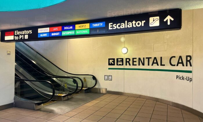 An escalator rises out of view; wall signage shows that it leads to the rental car pickup garage.